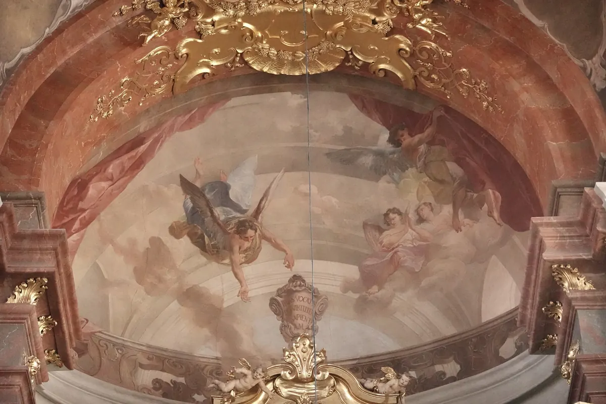A Baroque fresco in an arched bay of St Giles' Church, showing angels among clouds beneath a gilded stucco frame.