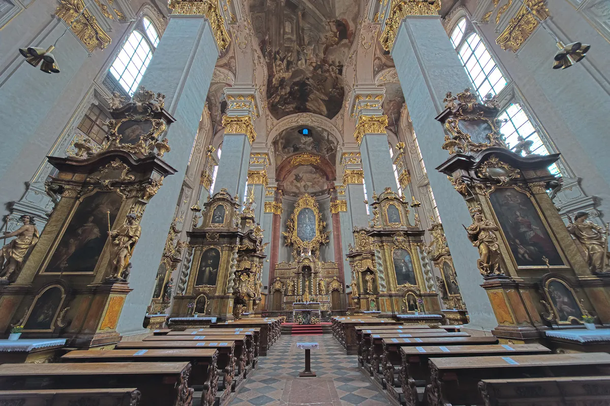 The nave of St Giles' Church seen from the aisle, with tall pale pillars, rows of wooden pews and gilded altars on both sides of the high altar.