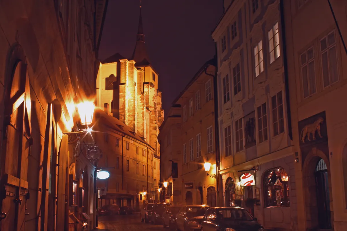 The tower and gable of St Giles' Church lit warmly at night above a narrow Old Town street with lamps and tall houses.