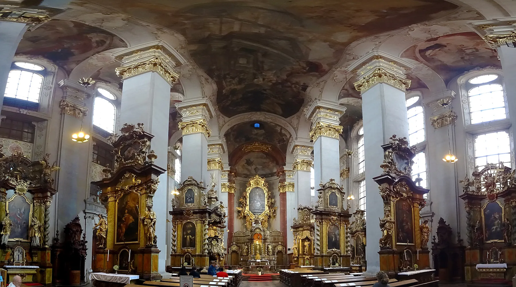 A wide view of the interior of St Giles' Church, with painted vaults overhead, pale pillars with gilded capitals and altars along the nave.